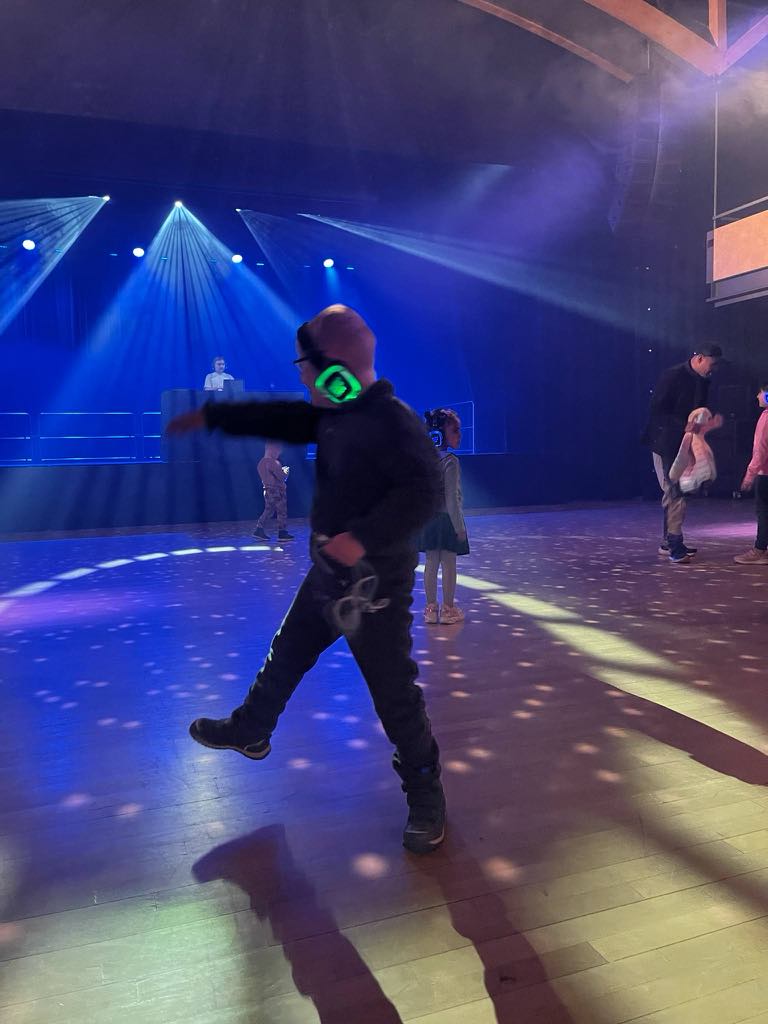 Min sønn danser på Silent Disco i en gymsal, som er mørk med discokule hengende i taket, som lager fargespill i gulvet