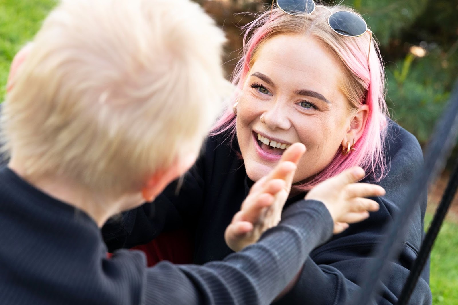 Nærbilde av en BPA-assistent med rosa hår som smiler og har øyekontakt med et barn utendørs.